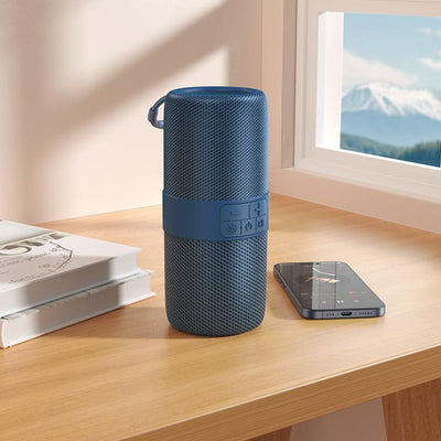 Blue portable speaker on a wooden surface with a phone and books